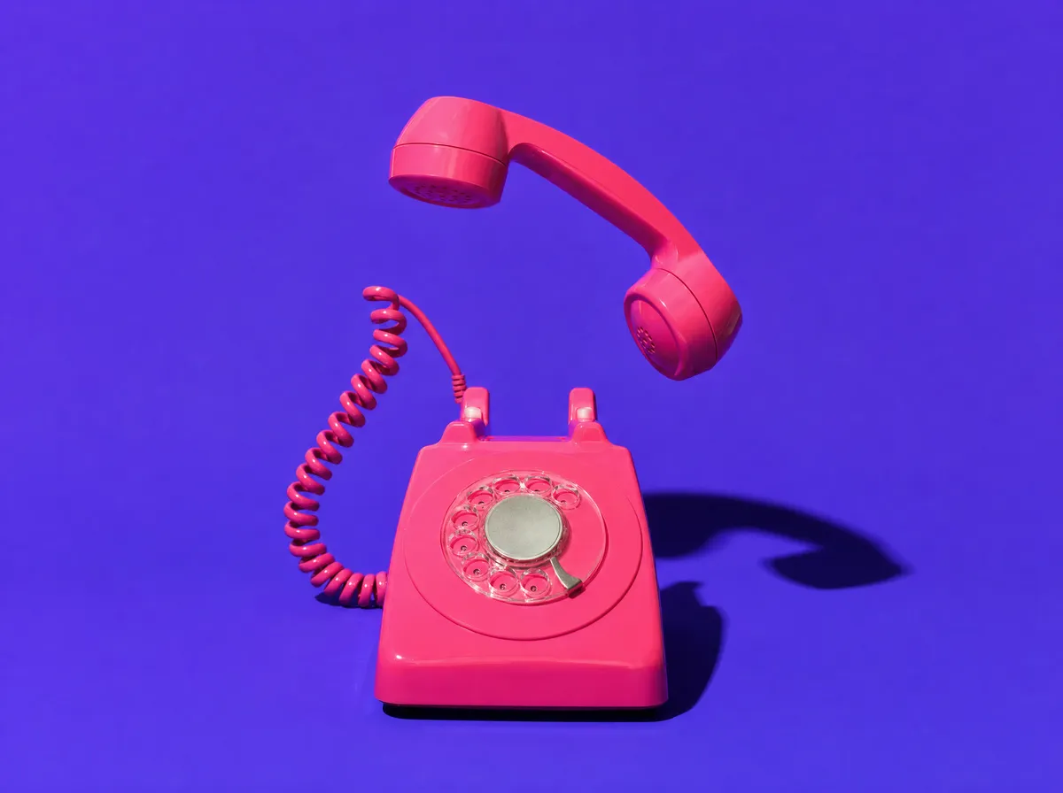 A pink rotary telephone with the handset lifted mid-air