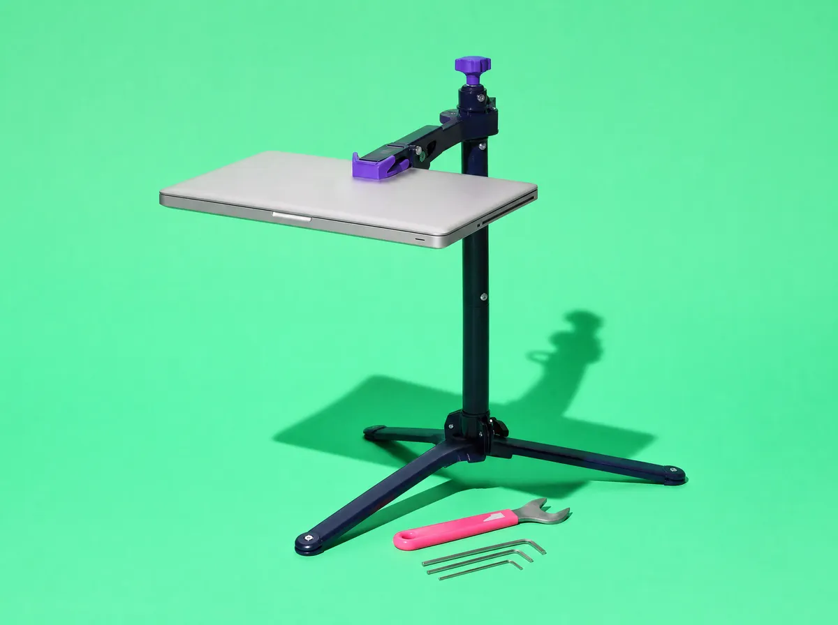 A laptop clamped in a bicycle repair stand, with a wrench and hex keys on the floor